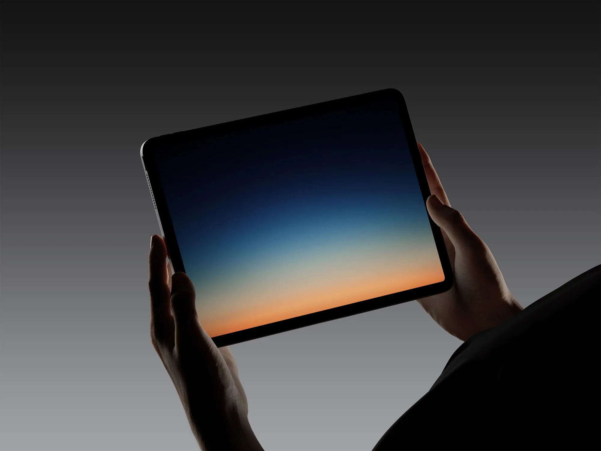 Ruce držící tablet se zobrazeným barevným přechodem na tmavém pozadí.